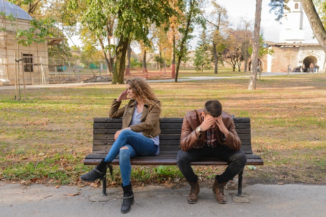 couple in a fight sitting on a park bench 