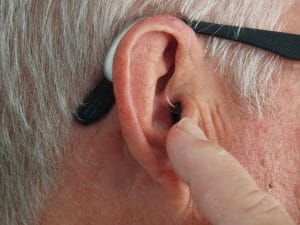 Main points at his hearing aid.