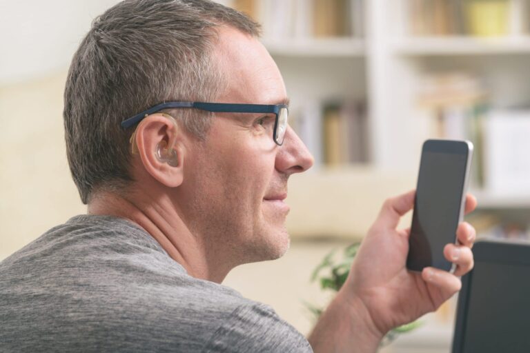 Man with hearing aid checks his phone.
