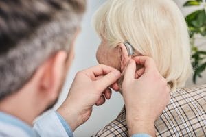 Audiologist inserting hearing aid on a woman's ear