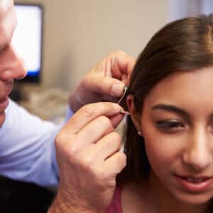 The hands of an audiologist fitting a young pesons hearing aid in profile