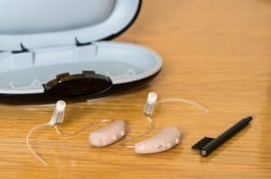 A pair of hearing aids next to a case and soft-bristled brush.